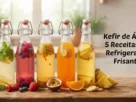 Foto horizontal de 5 garrafas de vidro com kefir de água de frutas e ervas sobre mesa rústica. No lado direito, o texto "Kefir de Água: 5 Receitas de Refrigerante Frisante".